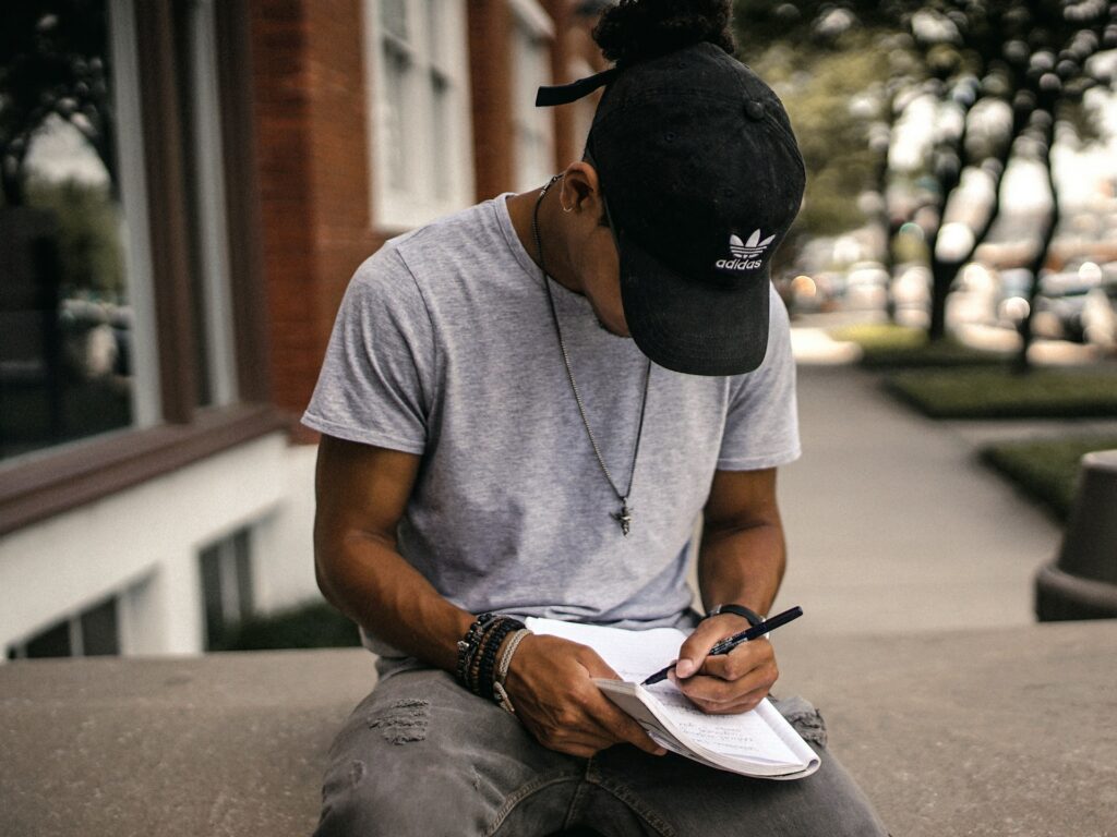Boy Sitting In Black Cap Writing