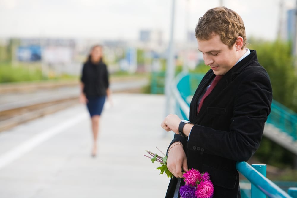 man-in-formal-attire-looking-at-watch-while-holding-flowers