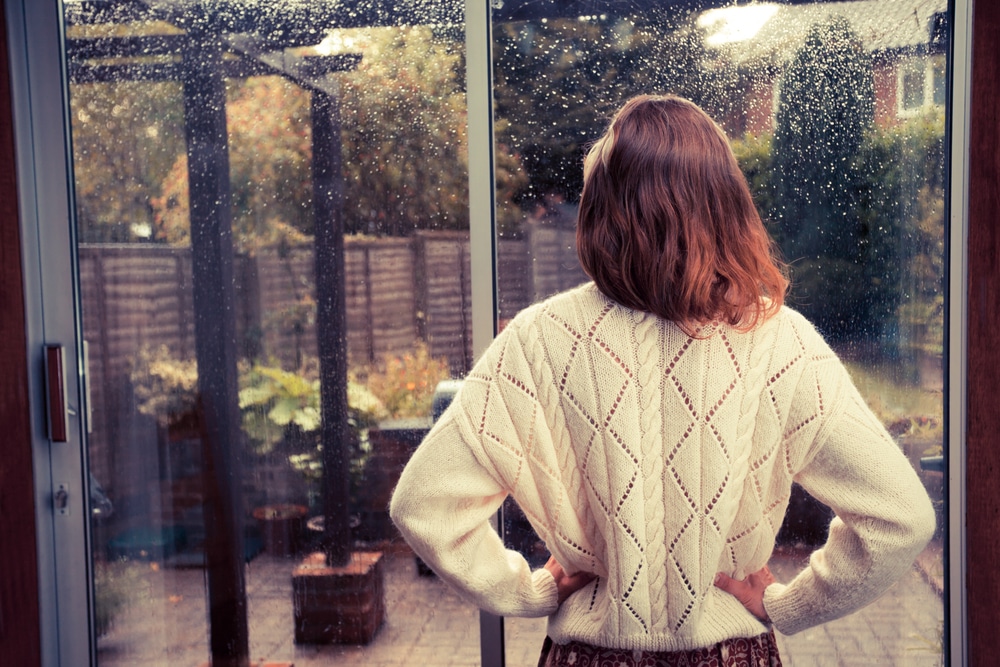 back-shot-of-red-haired-woman-looking-out-of-glass-door