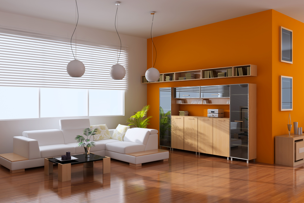 a-large-living-room-with-a-white-couch-by-a-coffee-table-with-hanging-lights-and-an-orange-wall-with-books-and-fixtures