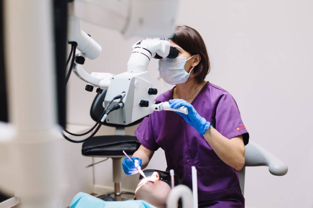 female-dentist-in-purple-scrub-using-dental-equipment-to-examine-a-patient