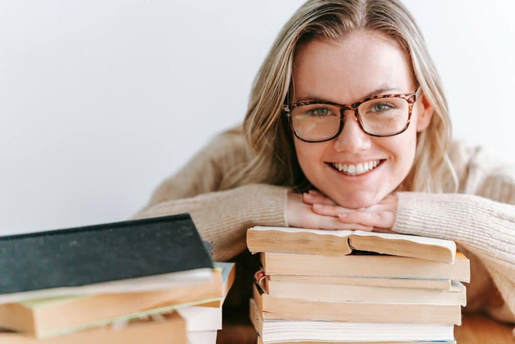 smiling-woman-in-glasses-resting-her-chin-on-stack-of-books