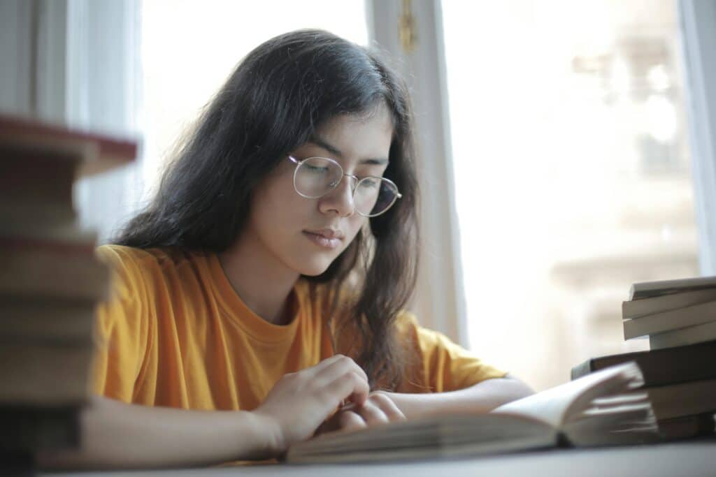 Girl in glasses reading a book at a table