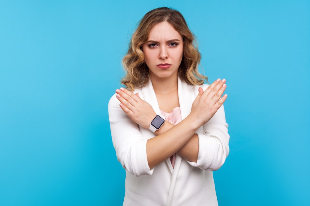 Woman signalling no with her arms crossed on a blue background