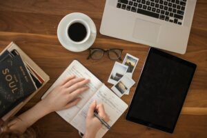 A woman writes in her notebook on a desk.