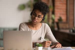 woman with glasses focused on her laptop and writing notes