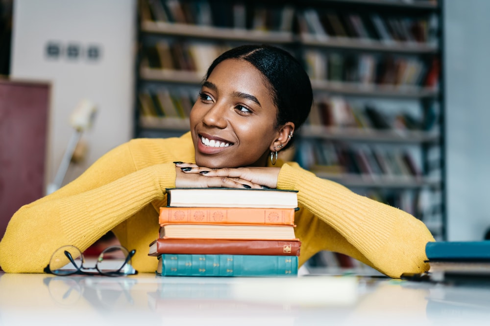 smiling woman resting chin and hands on a stack of books