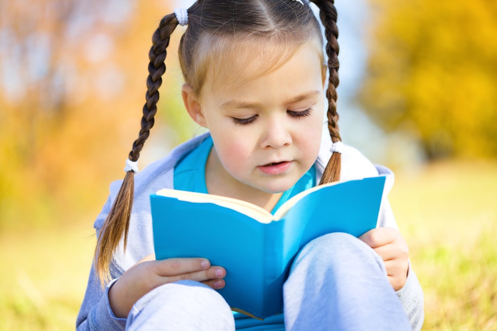 young girl reading a blue book outside