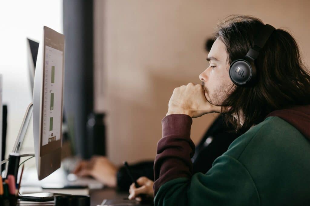 man in green cardigan listening to headphones on the computer