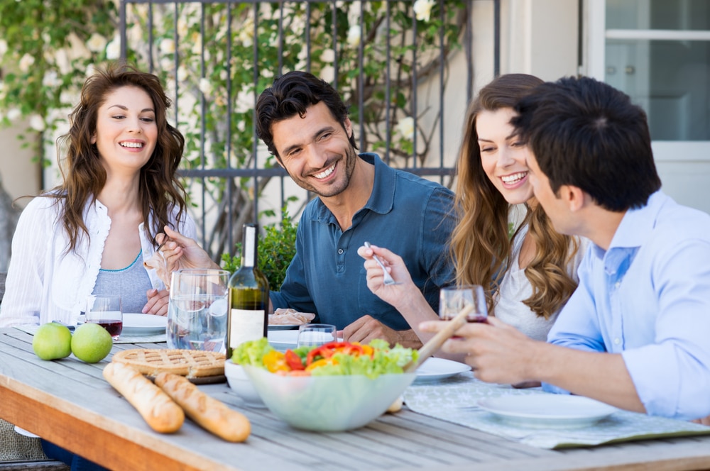 four adult friends eating together outside at a table