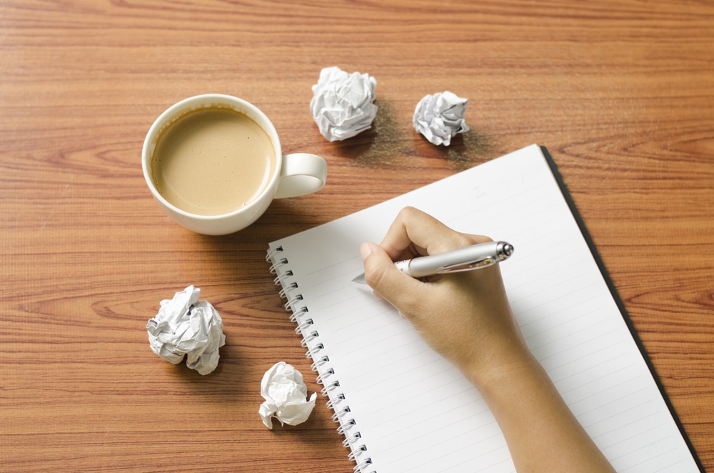 a hand holding a pen writing in a notebook on a wooden table