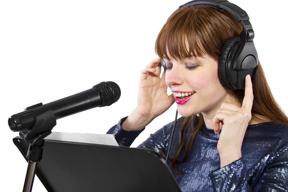 brunette woman with headphones on singing against a white background