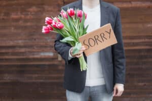 man holding tulips and cardboard sign saying sorry