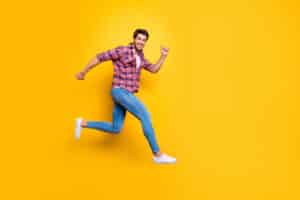 man in plaid and jeans jumping in the air against a yellow background