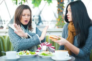 woman crossing her arms to say no to her friend while out for a meal