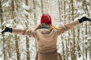 woman in the woods holding arms out to catch falling snow