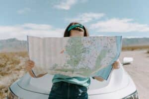 Woman sitting on the hood of a car looking at a map