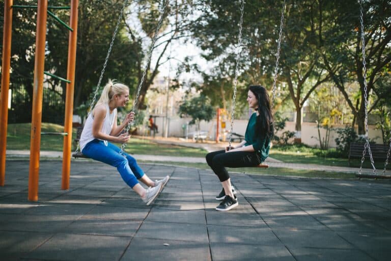 Two women talking while seated on swings