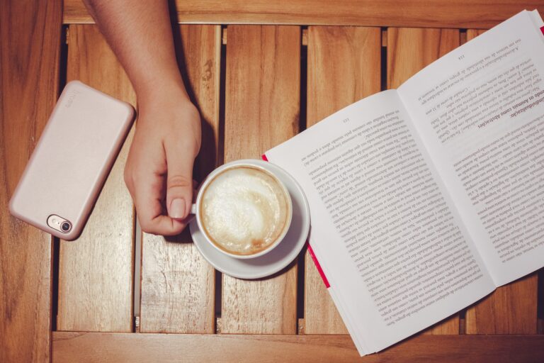 overhead-shot-of-hand-holding-coffee-mug-with-pink-smartphone-on-the-left-and-portuguese-book-on-the-right