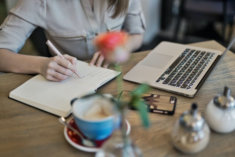 person-taking-notes-in-a-notebook-in-front-of-a-laptop