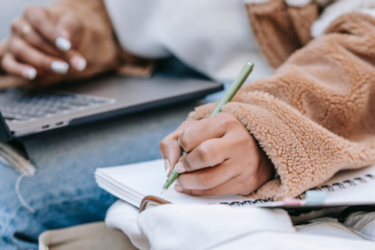 Person writing in notebook next to laptop