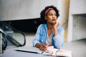 woman sitting at a table with her laptop and notebook thinking