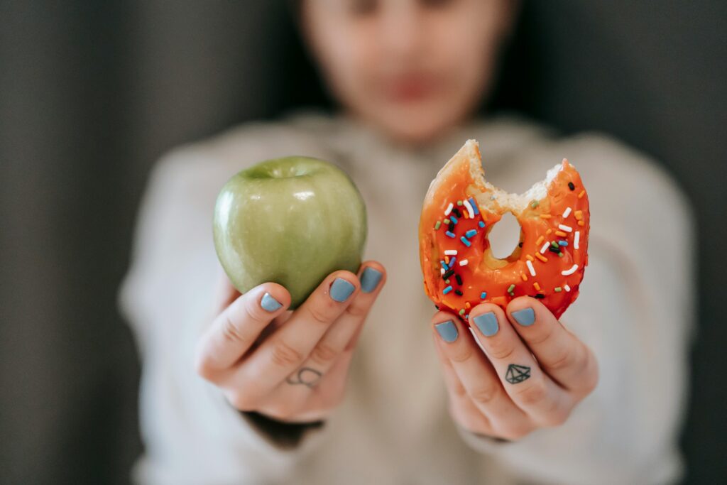 Photo by Andres Ayrton: https://www.pexels.com/photo/woman-showing-apple-and-bitten-doughnut-6551415/