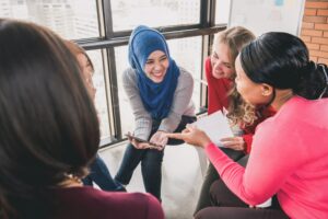 Diverse-women-sitting-in-circle-enjoying-sharing-stories-in-group-meeting