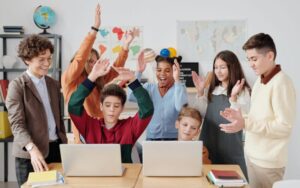 students and teacher looking excited at two laptops