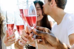 man kissing woman on the cheek while people are holding glasses of sparkling rose