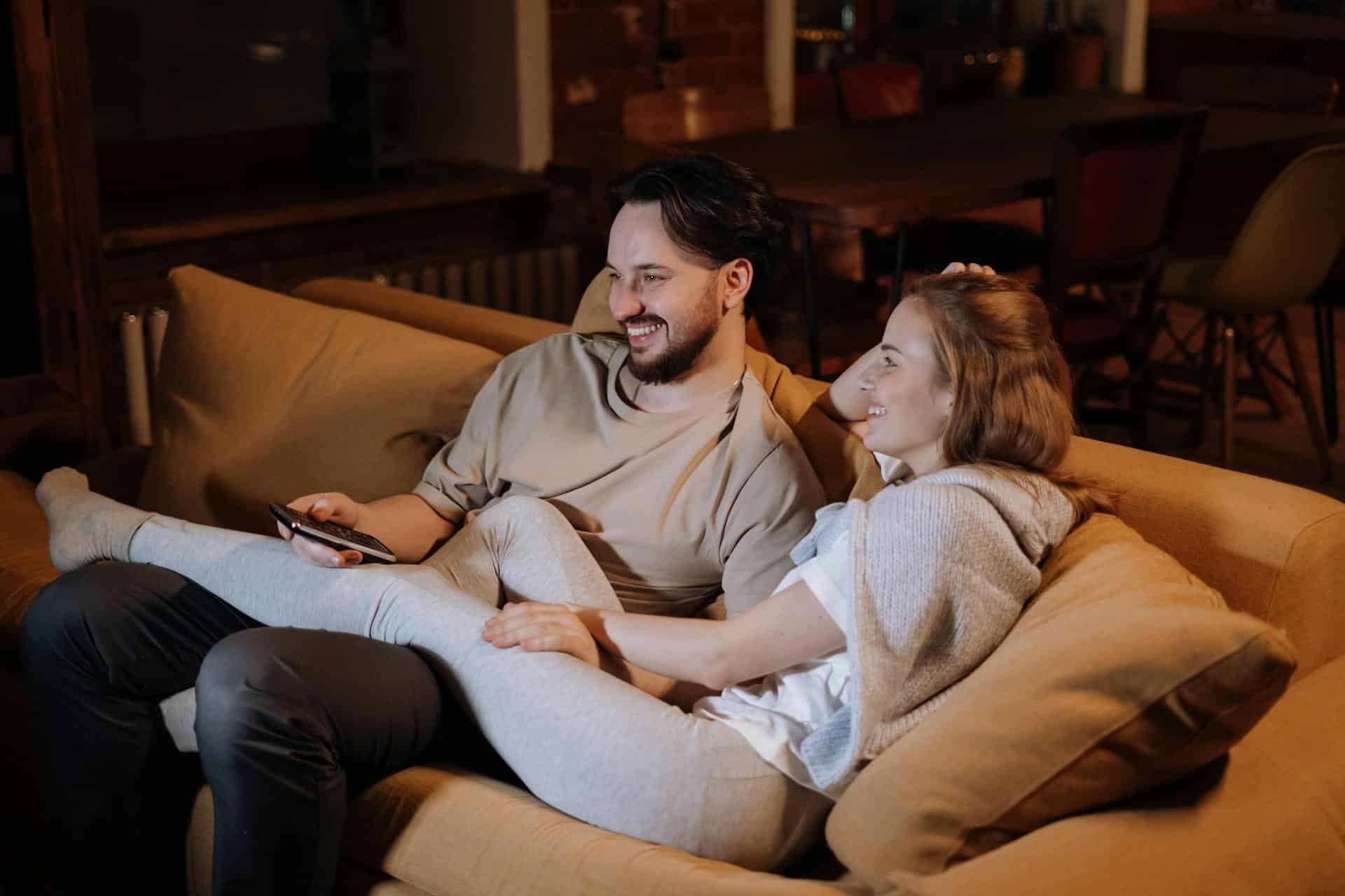 man-and-woman-sitting-on-couch-with-womans-legs-splayed-on-top-of-the-mans