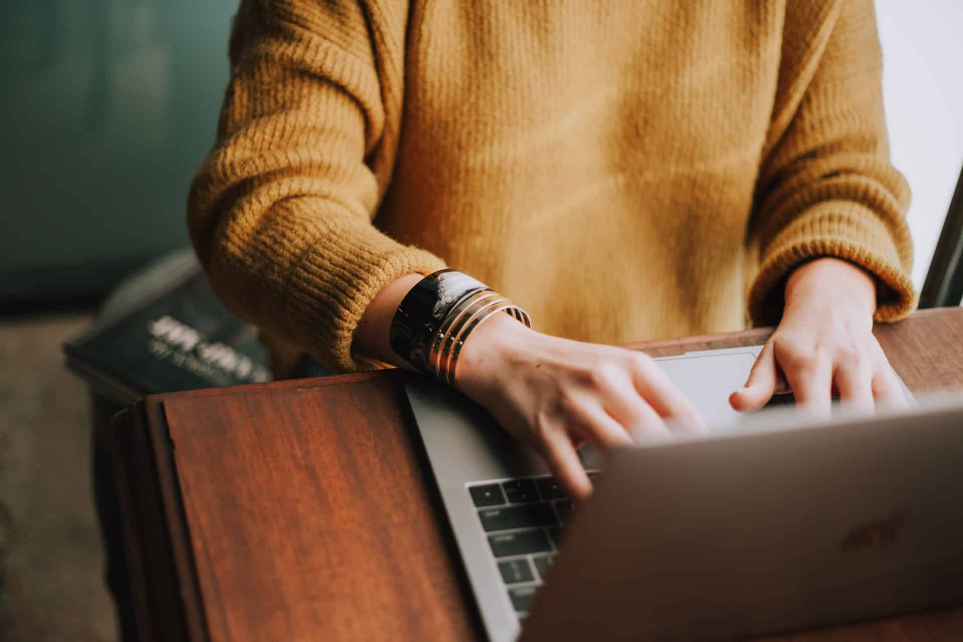 person in orange sweater working on their laptop