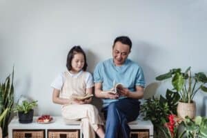 asian father and daughter reading on a bench