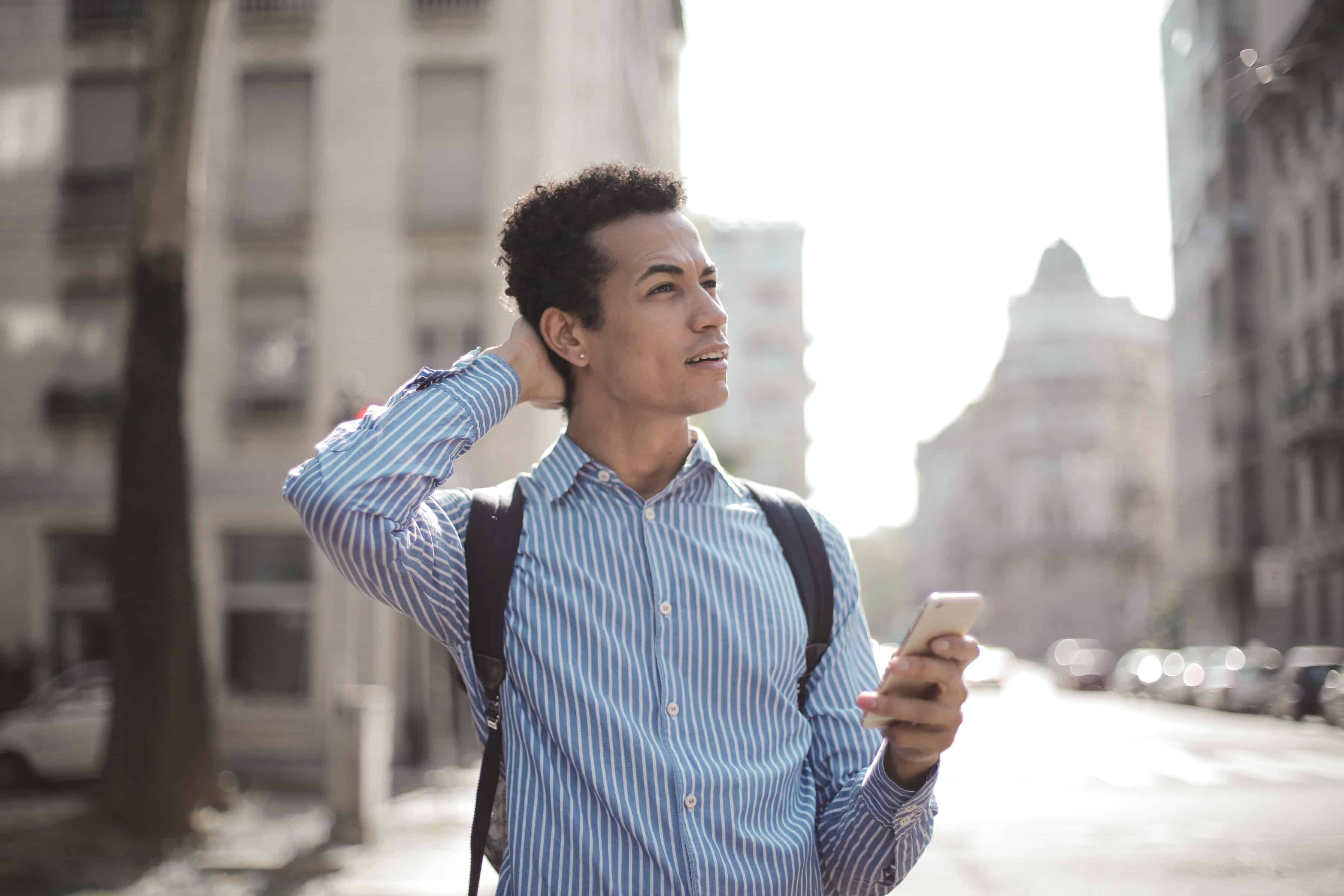 confused-worried-man-using-his-phone-in-the-street-while-looking-around-with-his-hand-on-the-back-of-his-head