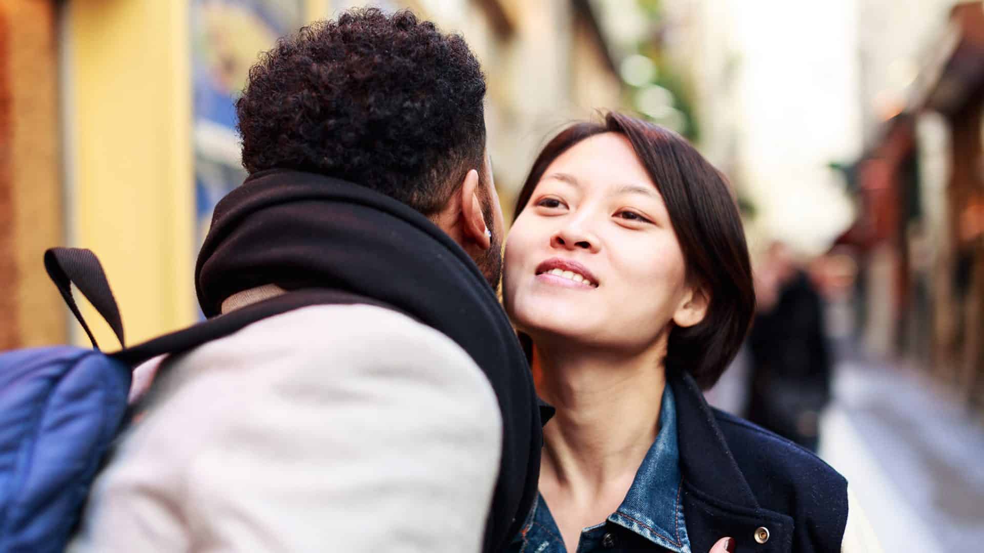 A couple greeting one another by kissing on the street.