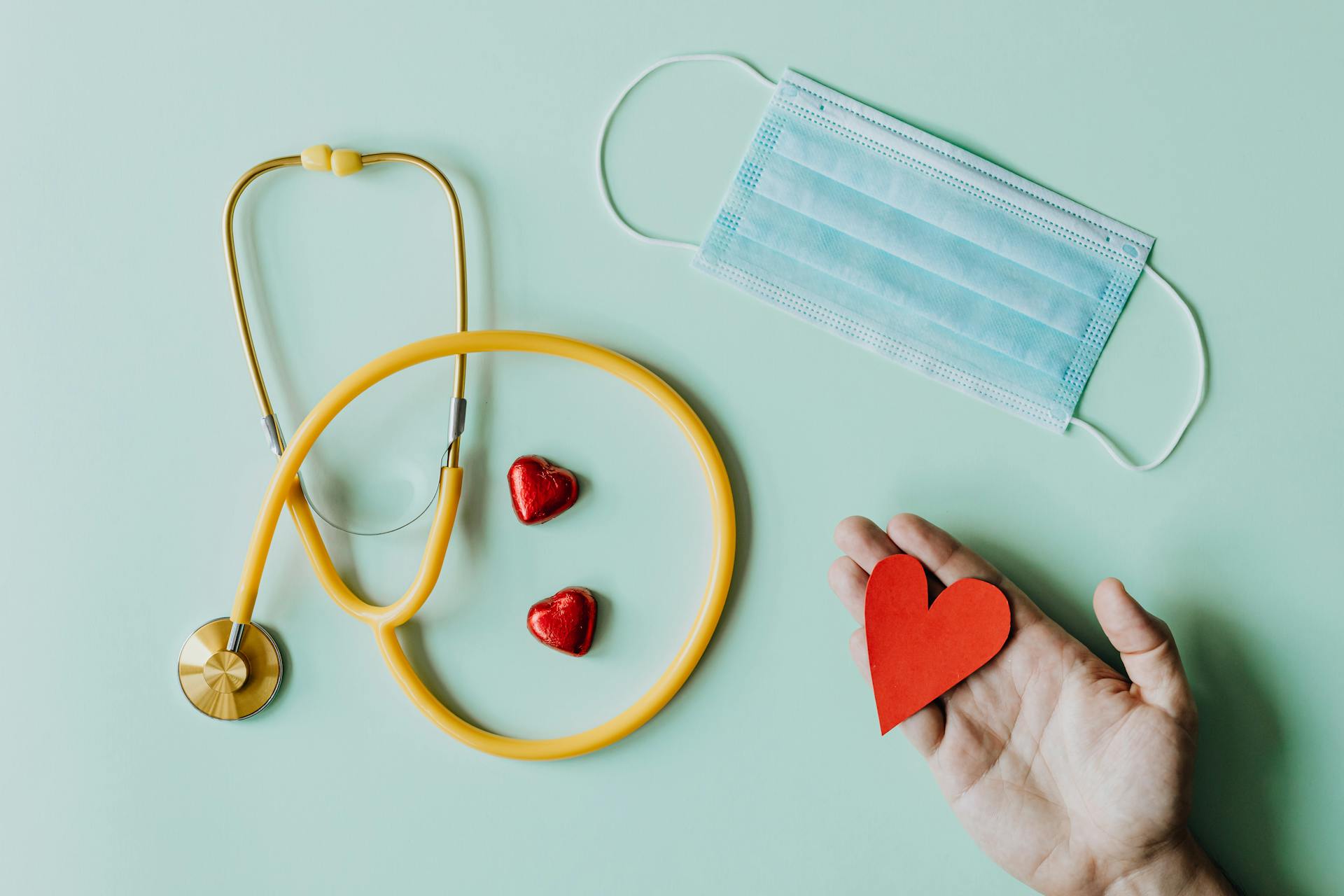 photo-of-stethoscope-face-mask-and-hand-holding-red-paper-heart