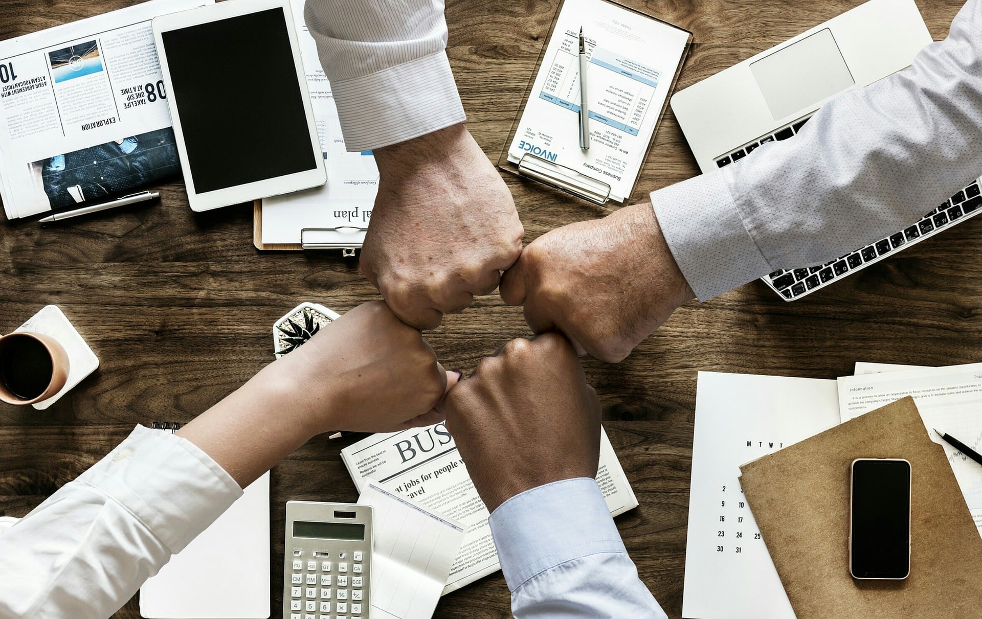 Four fists touching in center of the image over a table of financial tools.