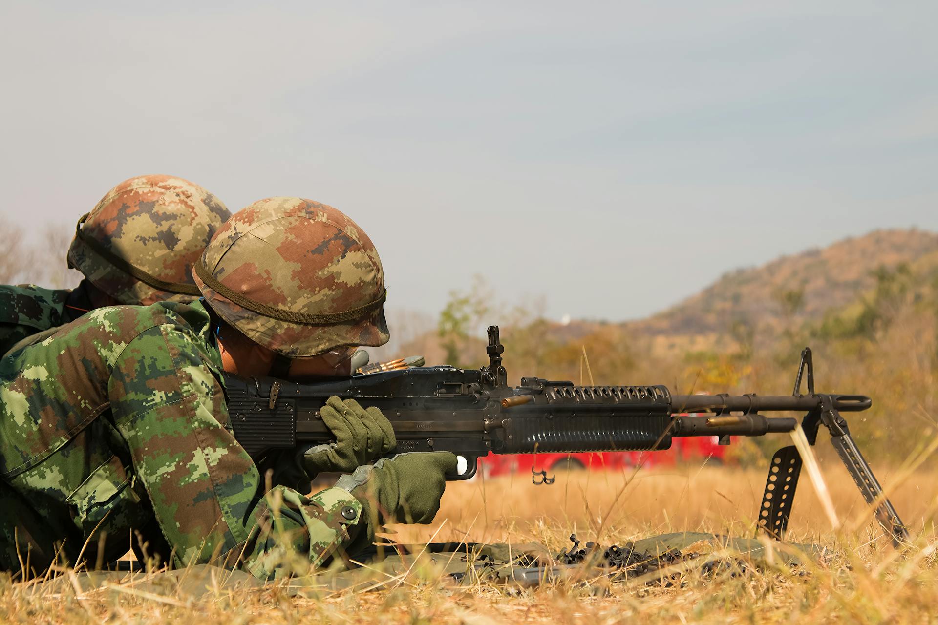 two-men-in-military-camouflage-attire-lying-belly-down-on-grass-and-positioning-rifle