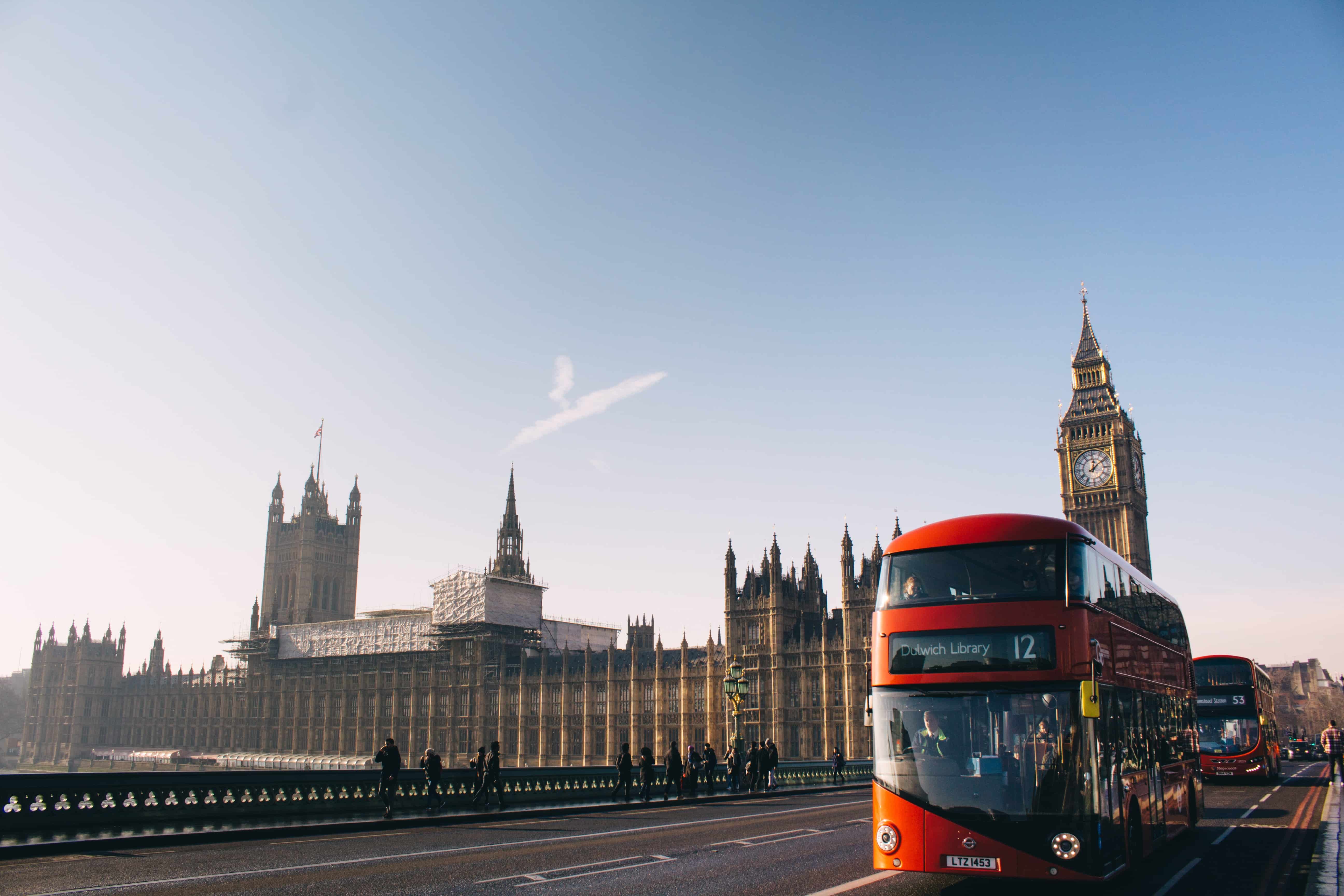 A red London bus travels in front of the Parliament building