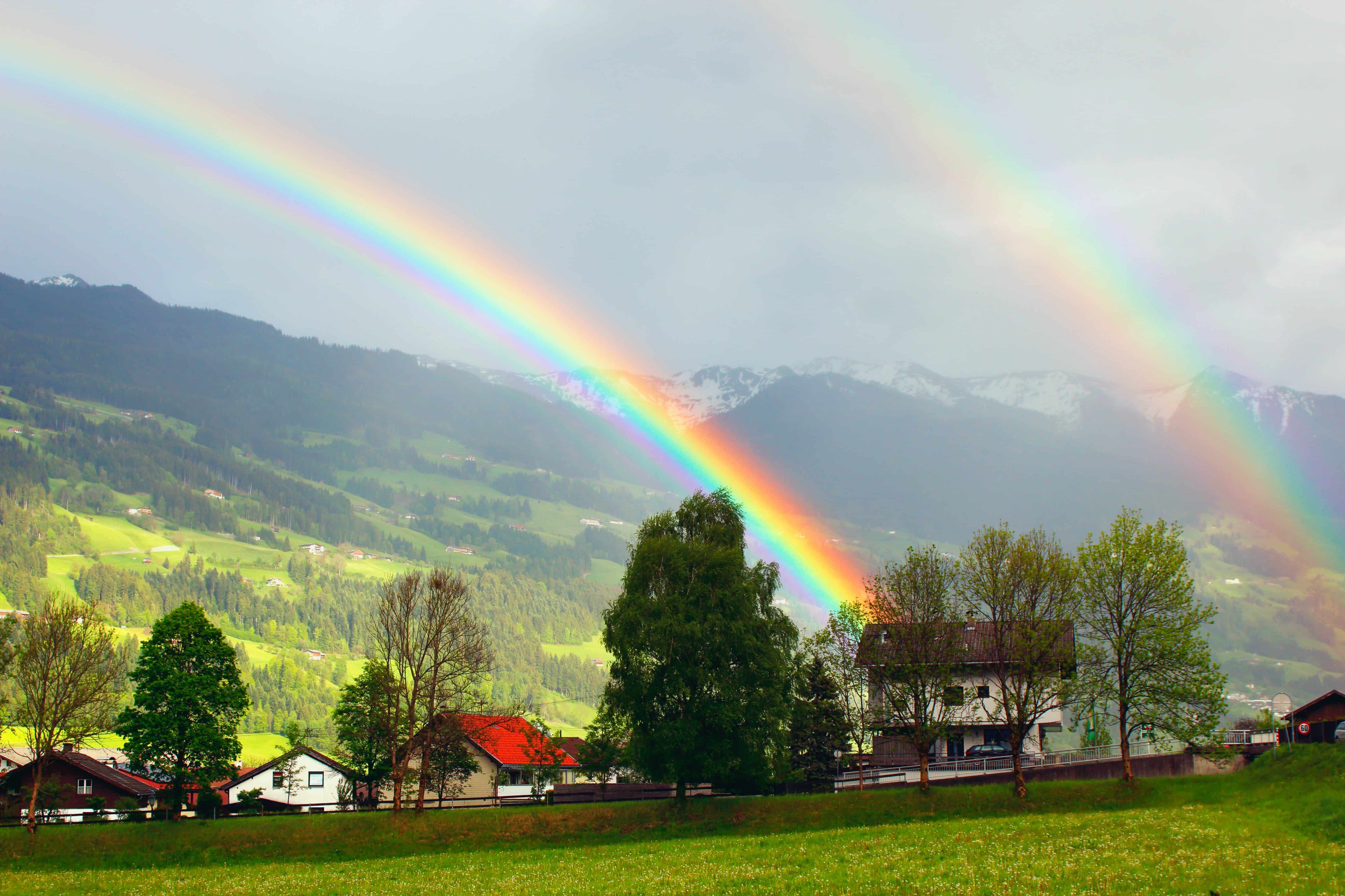 A vibrant double rainbow over a green field and a house