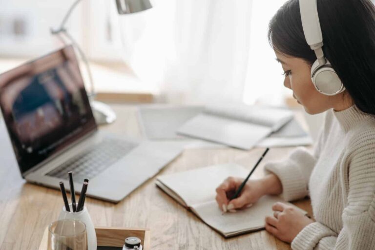 woman-listening-to-headphones-writing-in-notebook