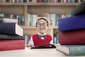 young smiling boy with glasses between two stacks of books in a library