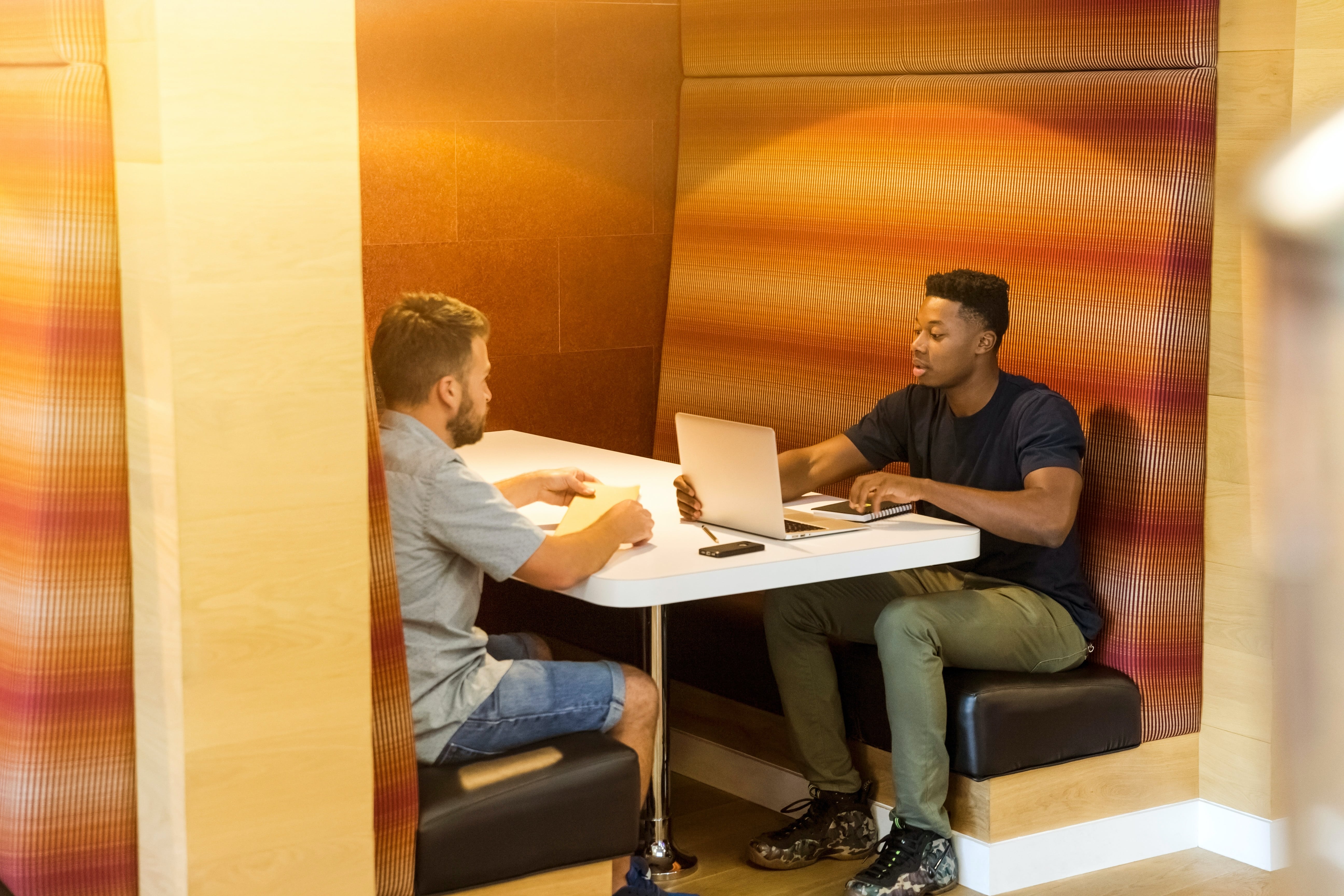 Two men work together in an office booth