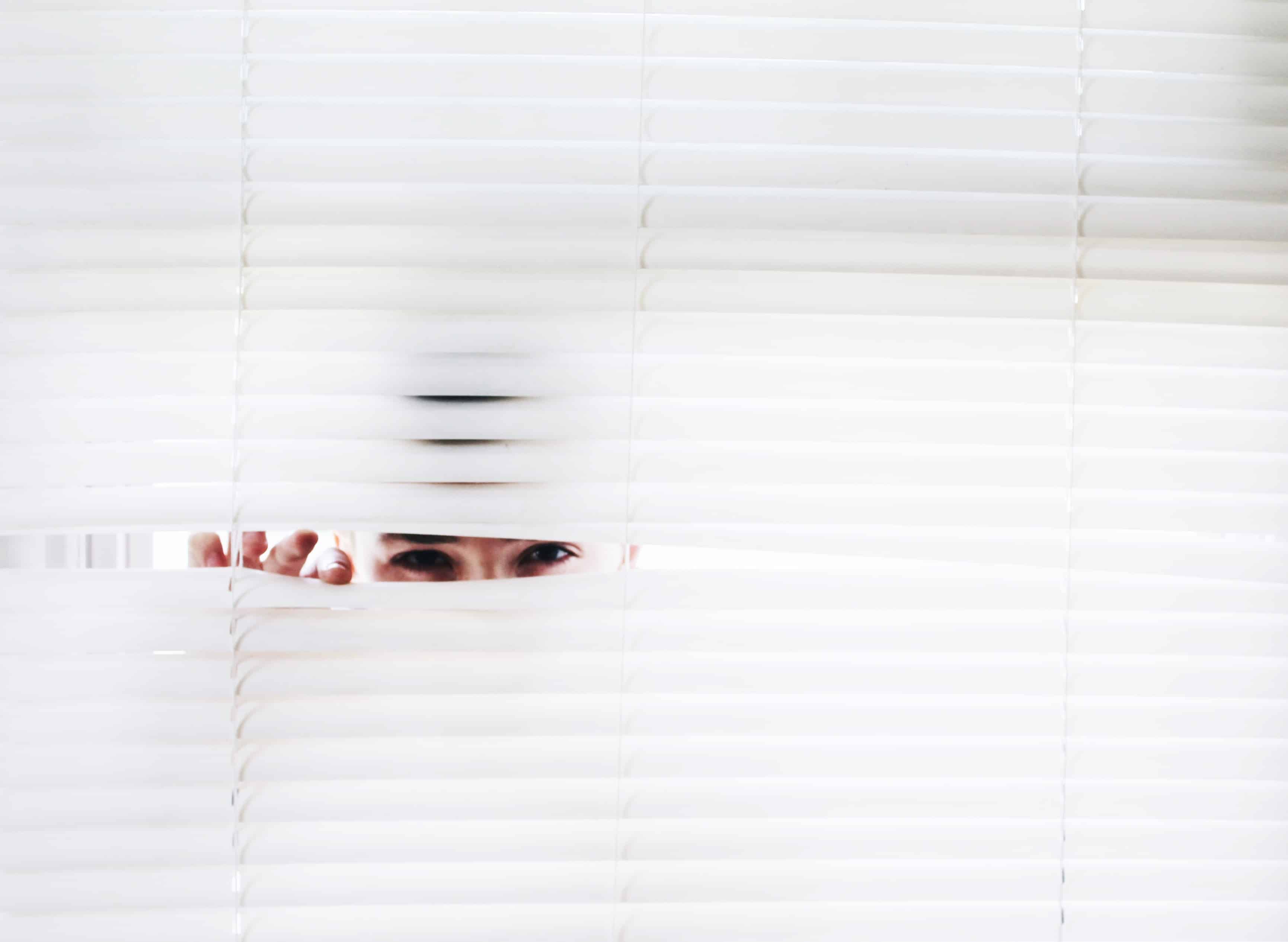 Person peeking through white blinds