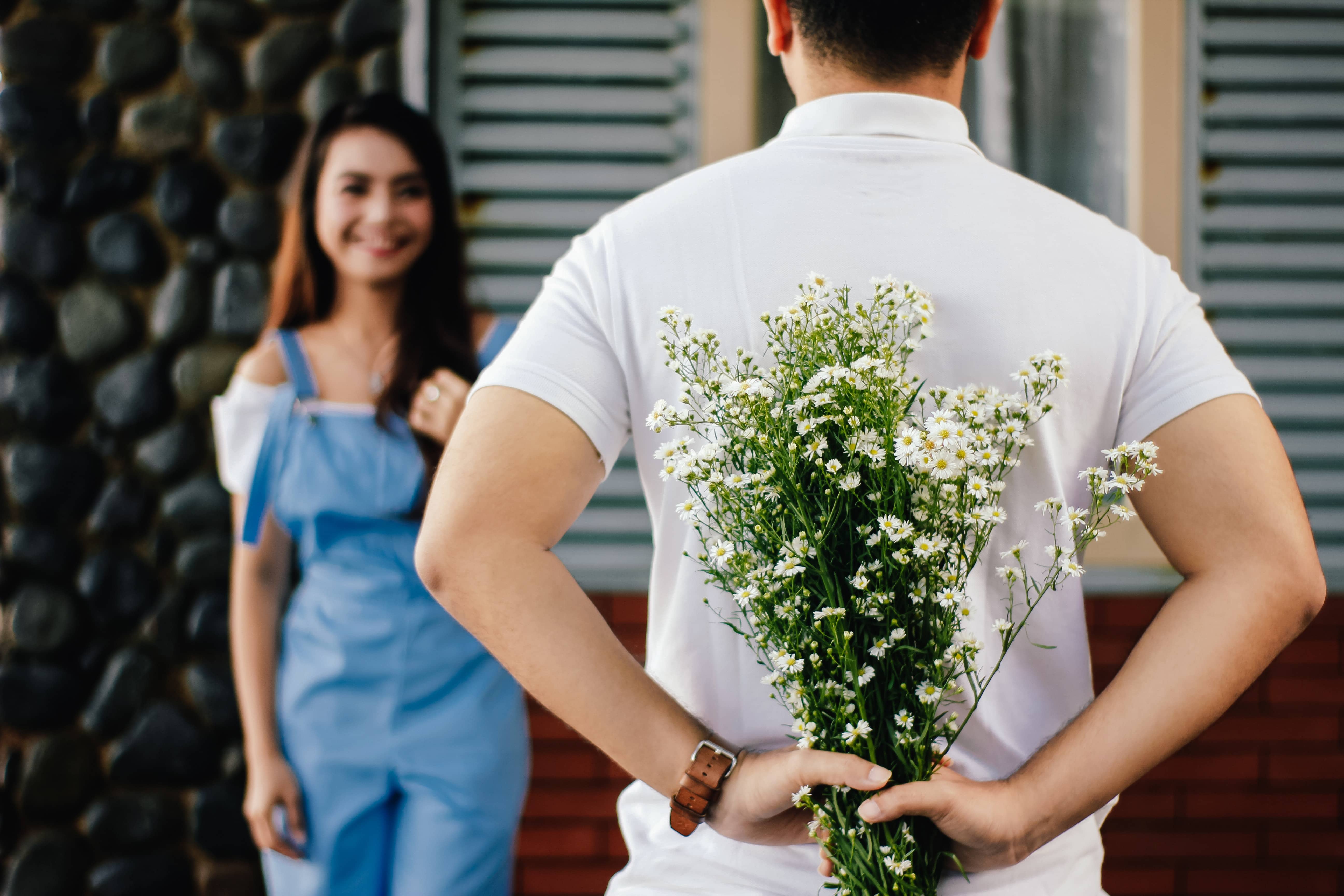 Man holding flowers behind his back in front of girl